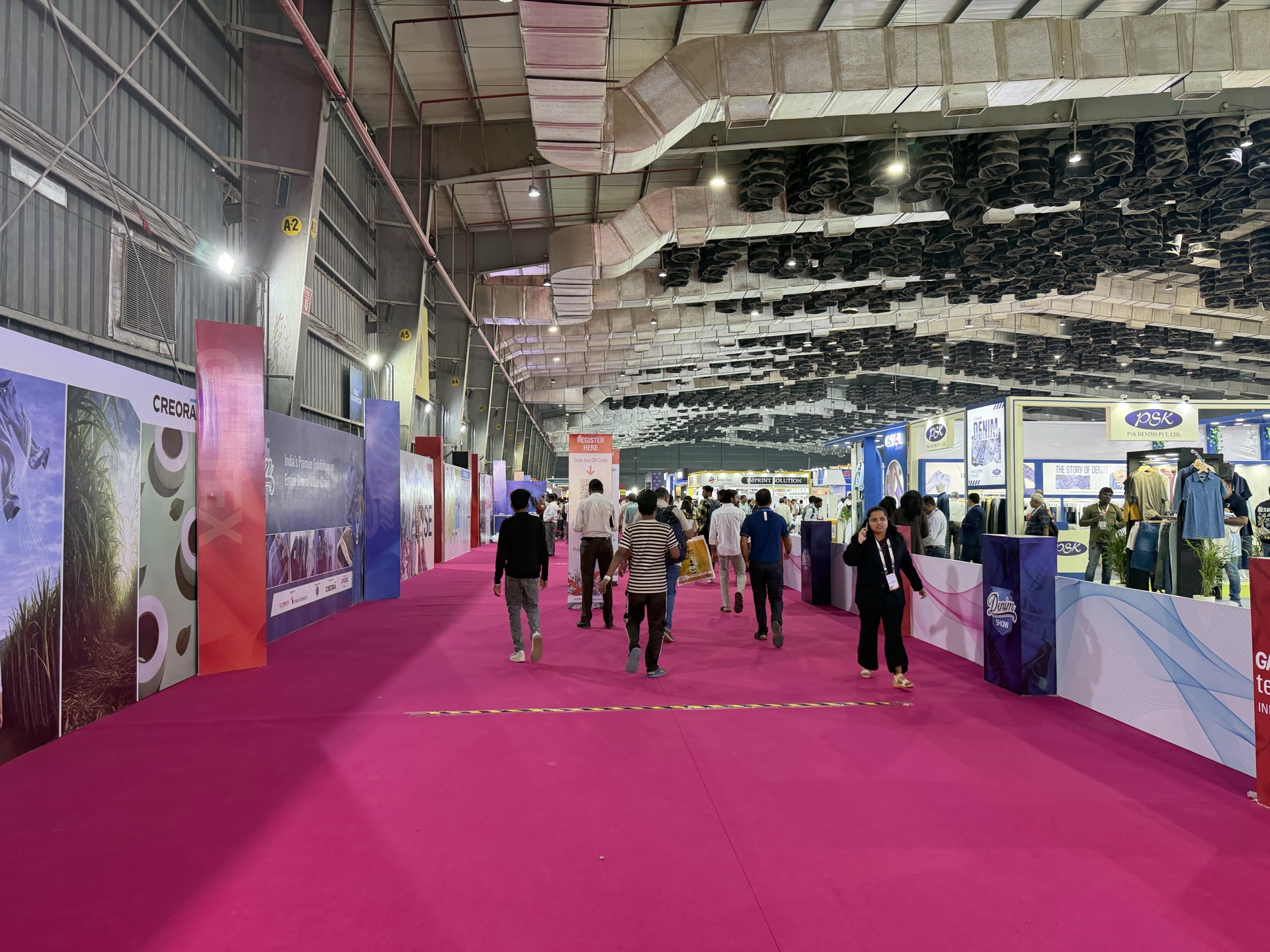 Magenta non-woven carpet covering the full Gartex exhibition hall — wide perspective showing carpet-defined floor at scale