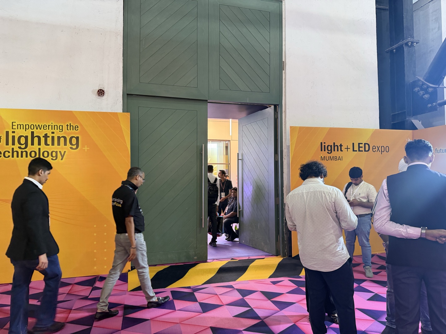 Visitor mid-stride crossing caution carpet at exhibition hall entry — Light + LED Expo Mumbai