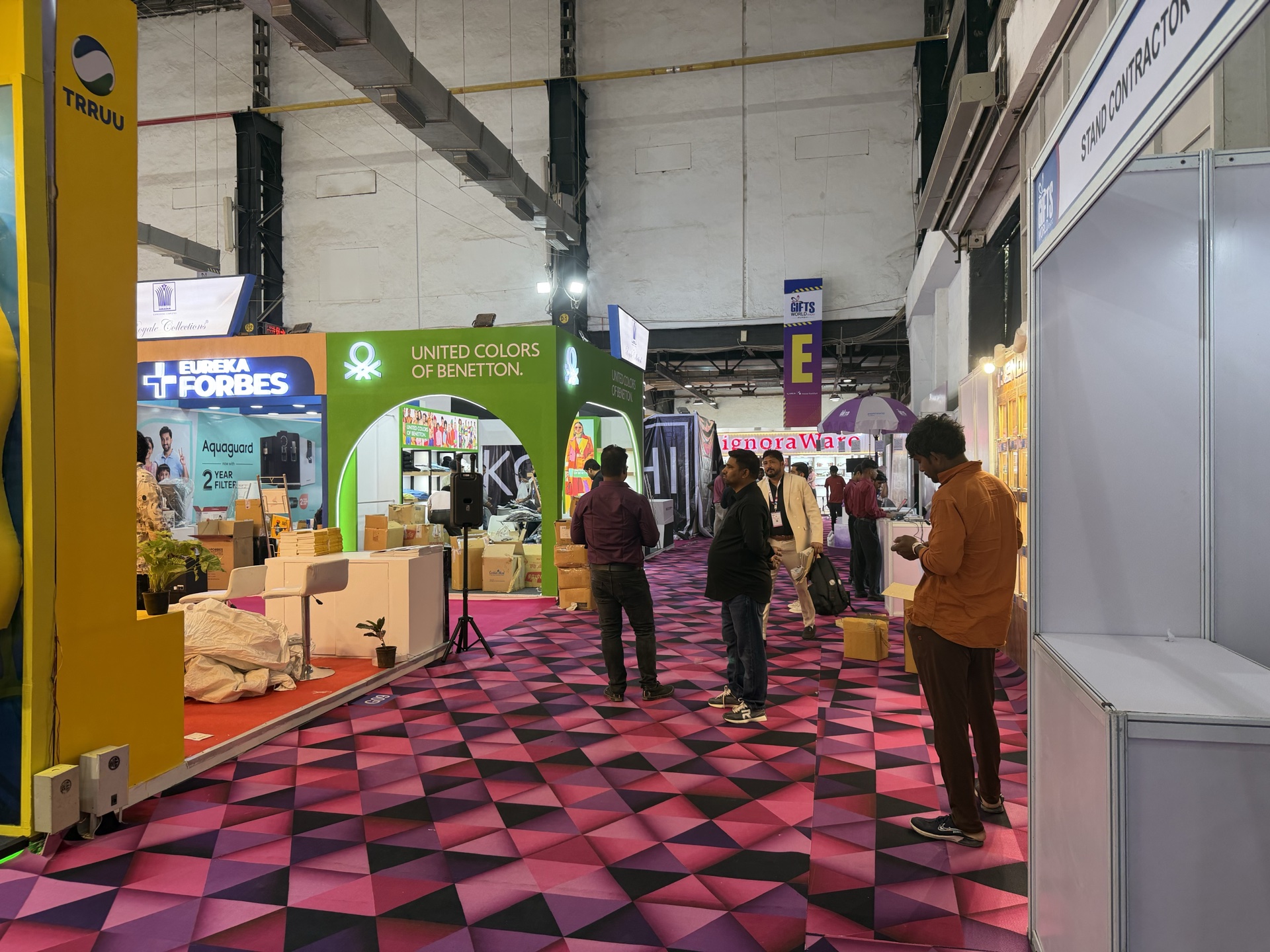 Wide exhibition hall floor covered end-to-end in a bold pink and magenta triangular geometric printed carpet at full architectural scale